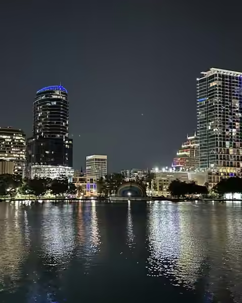 Downtown Orlando towers lit up at night, reflected in Lake Eola